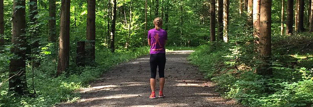 Outdoor Training auch im Grünen rund um Affoltern am Albis Frau mit Zopf im Sportoutfit von hinten auf einem Waldweg bei Sonnenschein.