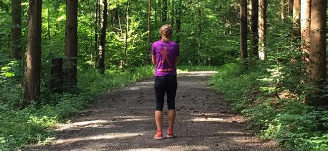 Outdoor Training auch im Grünen rund um Affoltern am Albis Frau mit Zopf im Sportoutfit von hinten auf einem Waldweg bei Sonnenschein.